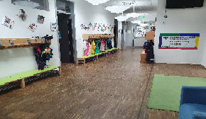 Das Bild zeigt einen Gang, mit einer langen Garderobe an der Wand mit Bildern der Kinder darüber, sowie einem kleinen grünen Teppich.